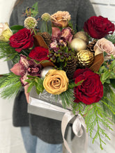 Load image into Gallery viewer, A bouquet of flowers including red roses, golden confetti, and greenery, presented in a clear container with a silver ribbon.
