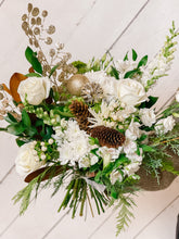 Load image into Gallery viewer, a winter flower bouquet with white roses, winter greens, pinecones, and ornaments held against a white backdrop.
