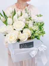 Load image into Gallery viewer, A person holding a large white floral arrangement in a rectangular box with a ribbon, containing white roses, tulips, and other premium flowers.