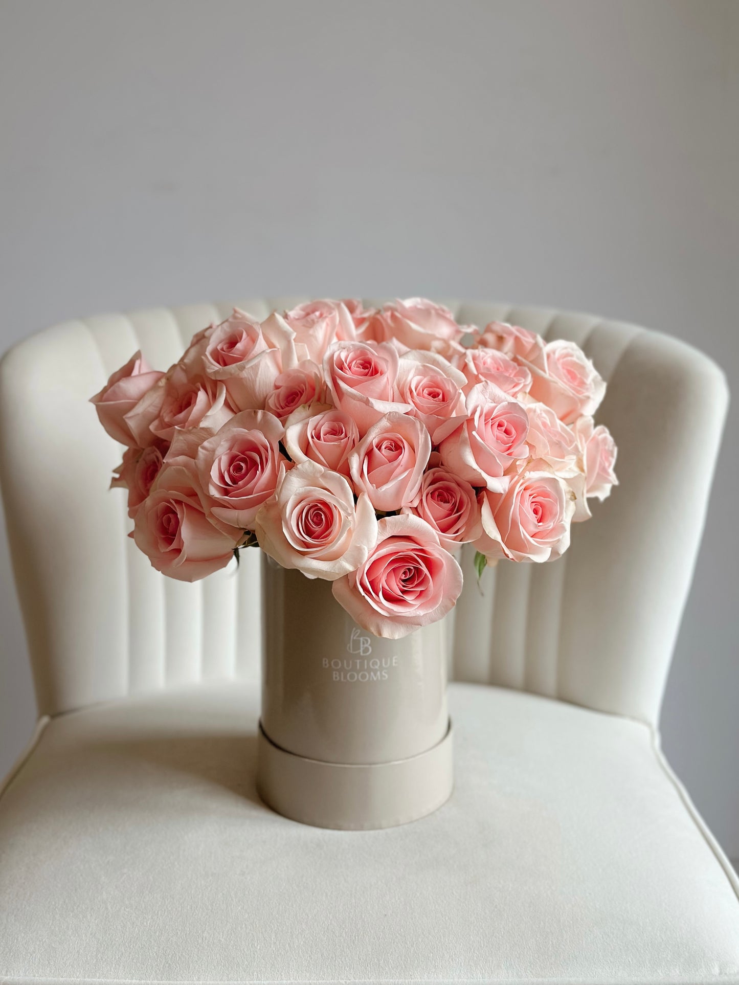 Bouquet of pink roses in a taupe box on a white chair with a light gray background