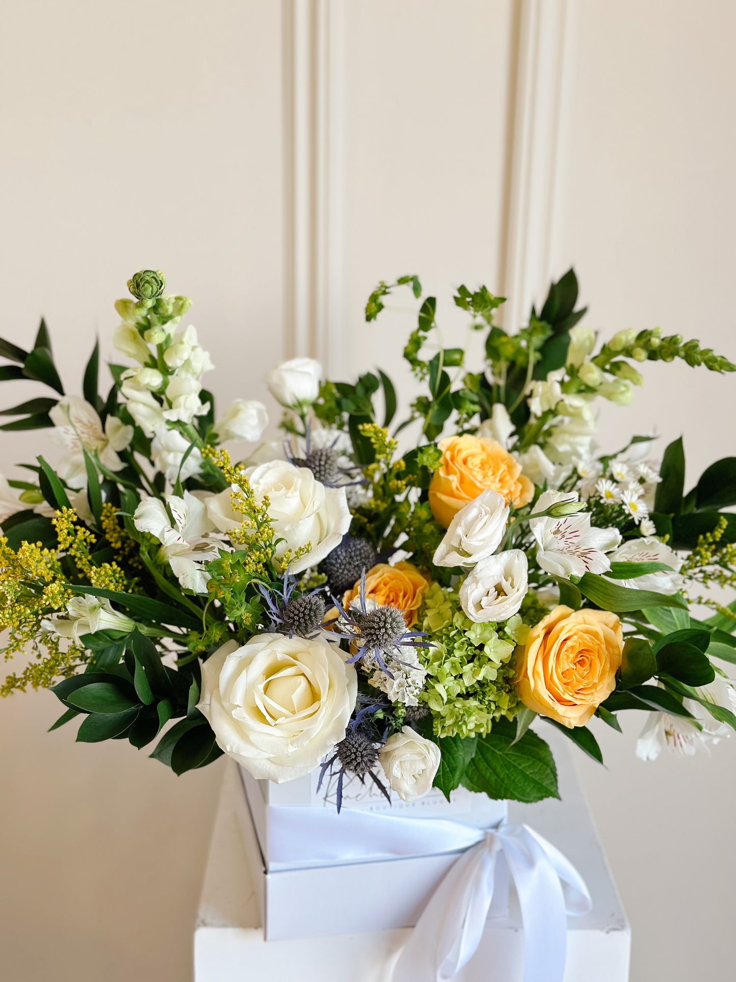 A vibrant floral arrangement featuring a mix of yellow and white flowers in a white box set against a neutral background.