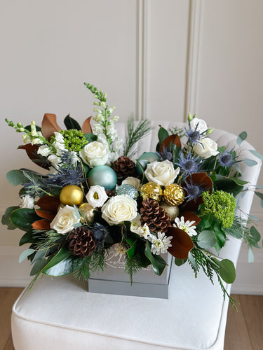 Decorative floral arrangement with greenery, white flowers, and gold ornaments on a white surface.