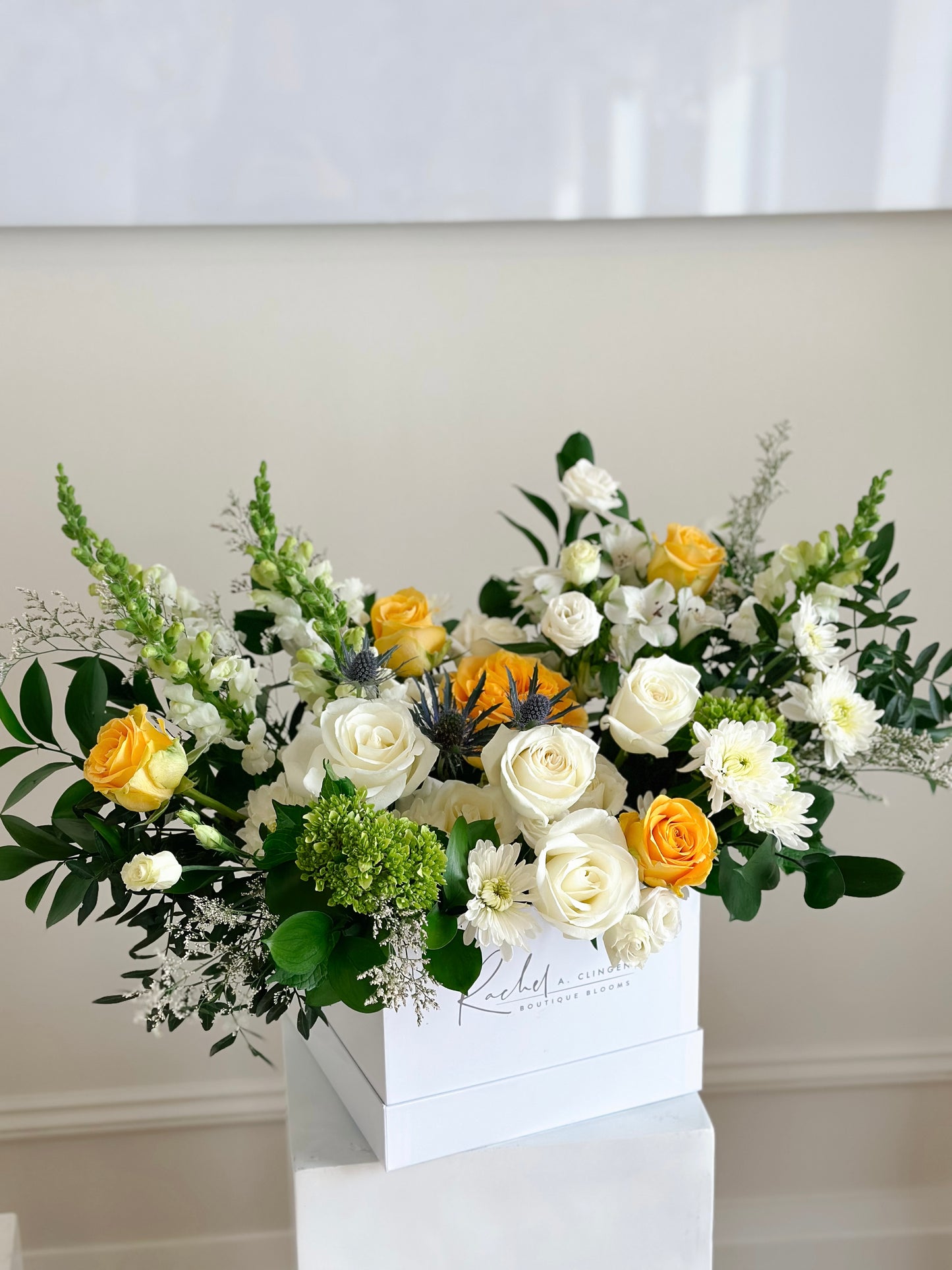 A large floral arrangement featuring a mix of yellow and white flowers in an extra large white square box, set against a neutral background.