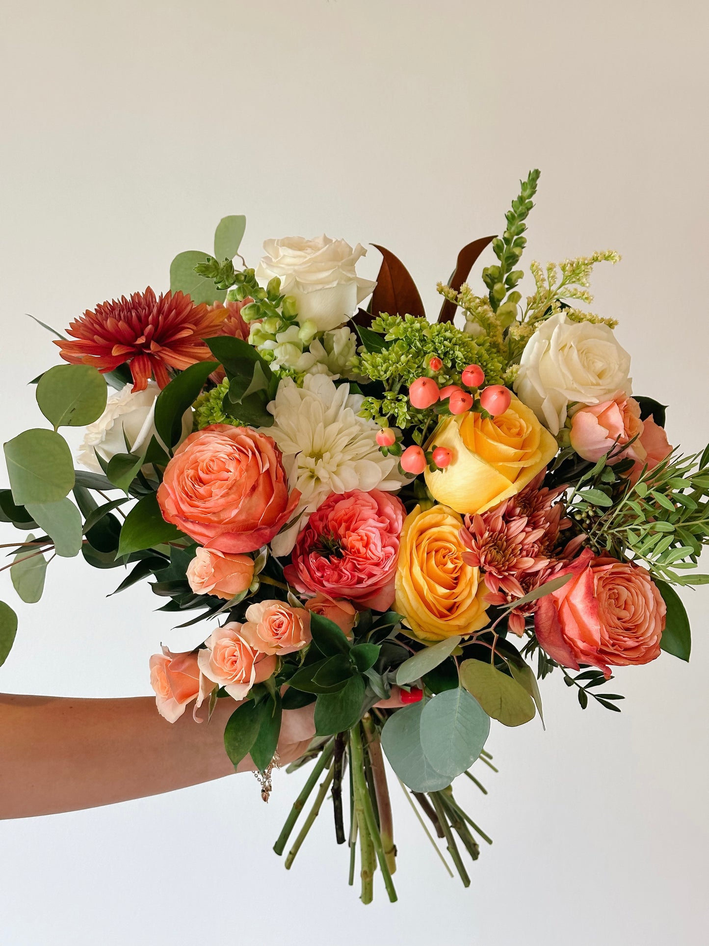 a flower bouquet with a rusty color palette including peach roses, yellow roses, and magnolia leaves.