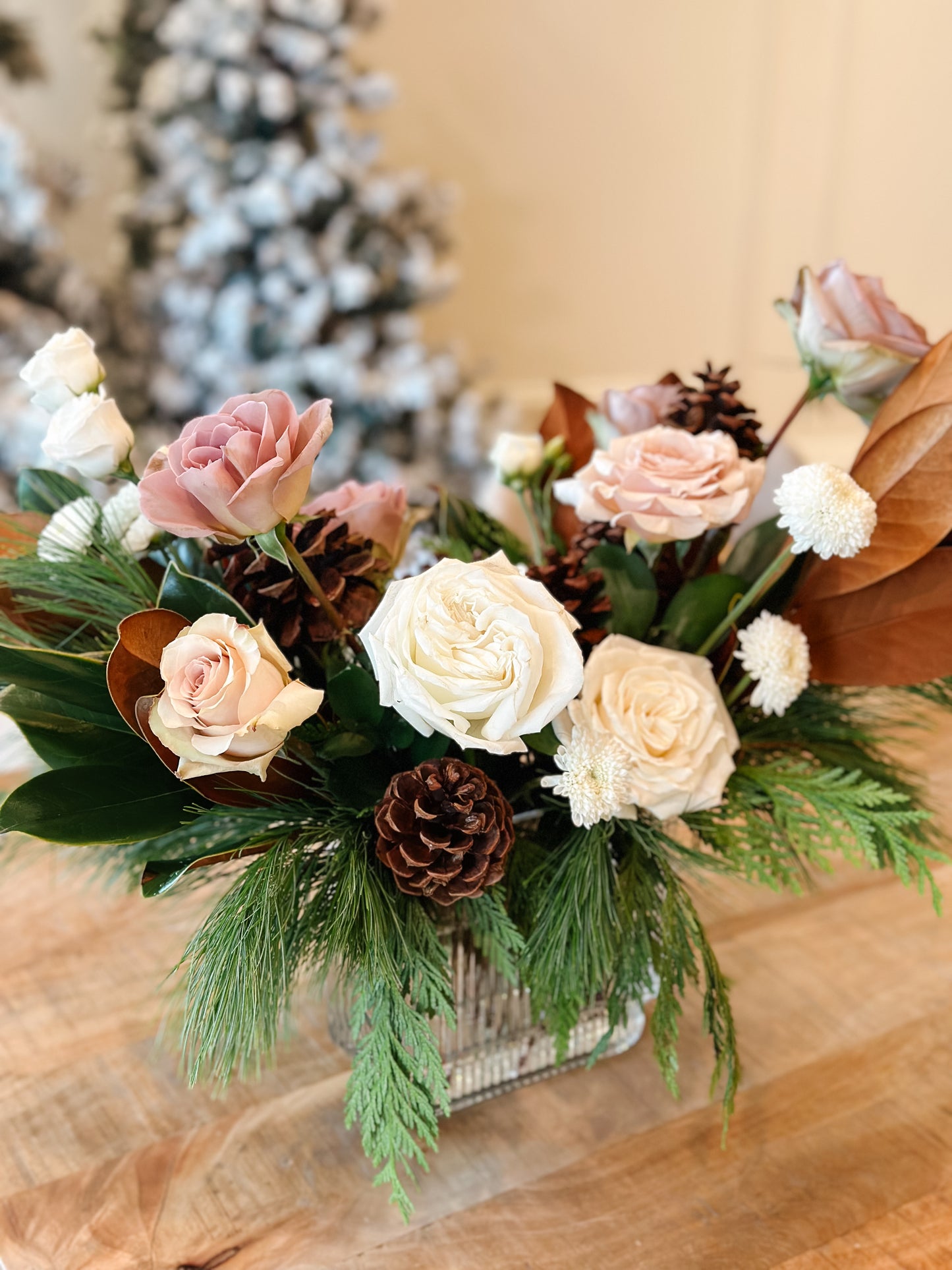Floral arrangement with roses, pinecones, and greenery on a wooden surface.