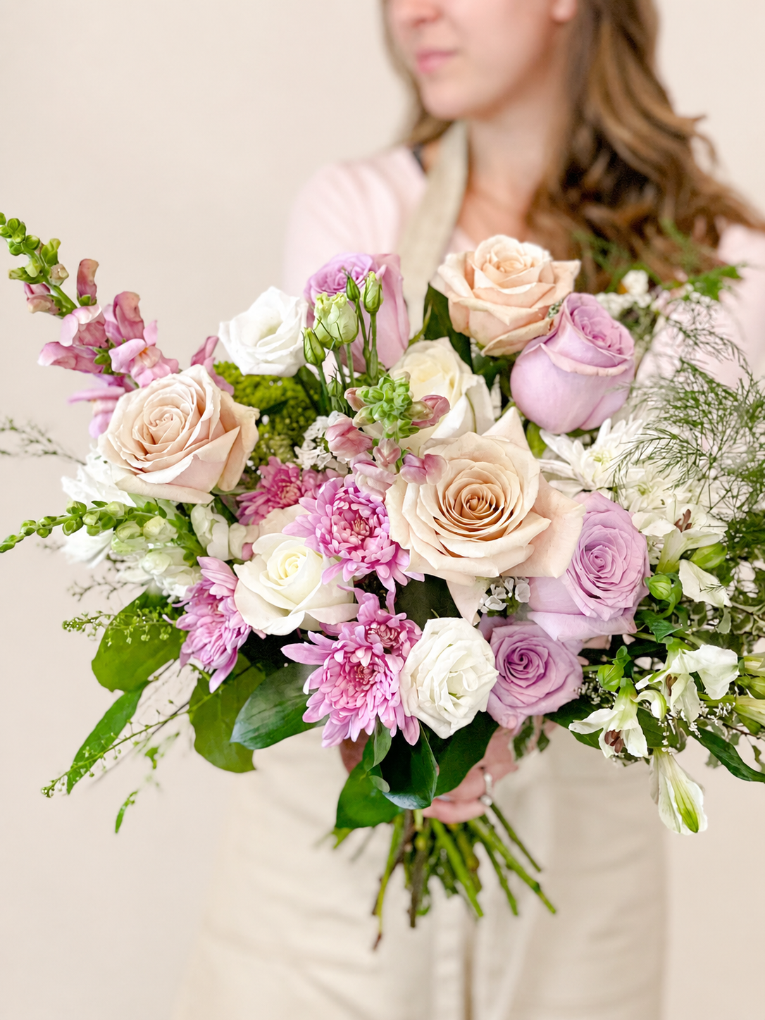 Bouquet of pink, white, and purple flowers held by a person against a neutral background