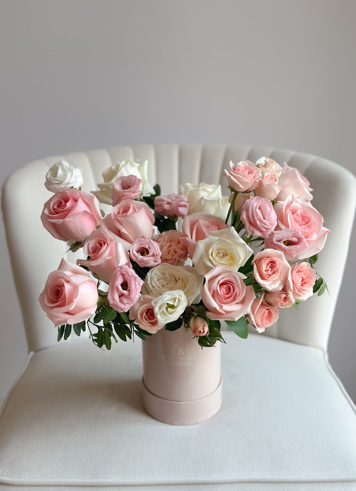 Bouquet of pink and white roses in a pink box on a white chair.