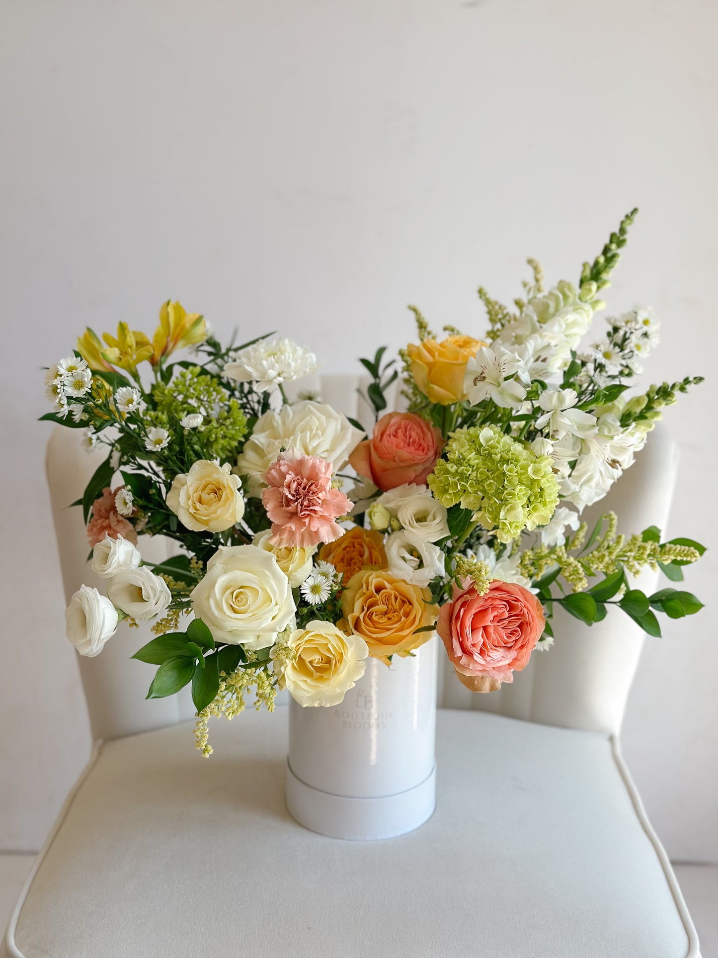 Pastel roses, hydrangea, and seasonal blooms arranged in a modern white floral box with fresh greenery.