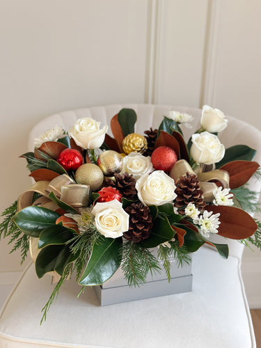 Decorative floral arrangement with flowers, pinecones, and ornaments on a white chair.