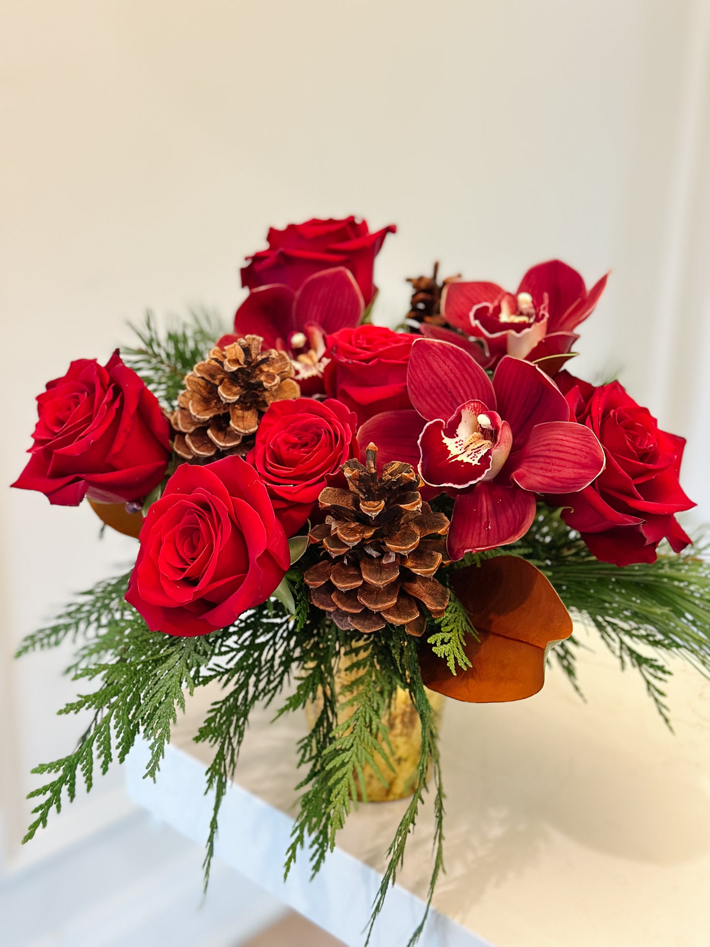 Bouquet of red flowers with pine cones and greenery on a white surface.