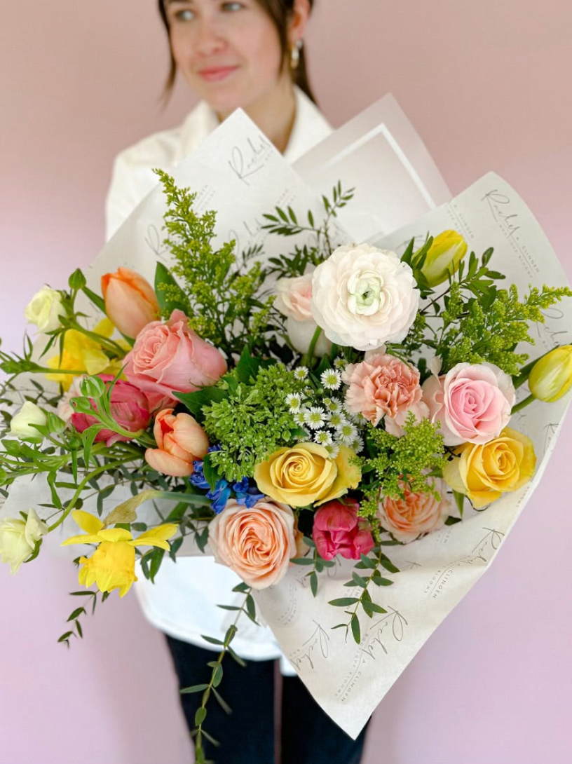 Bouquet of flowers held by a person against a pink background