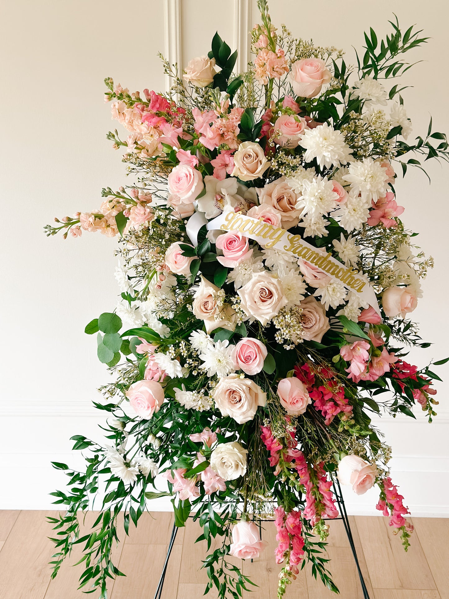 A standing sympathy spray arranged with a variety of fresh flowers including roses and other floral blooms in shades of pink, white, and green.