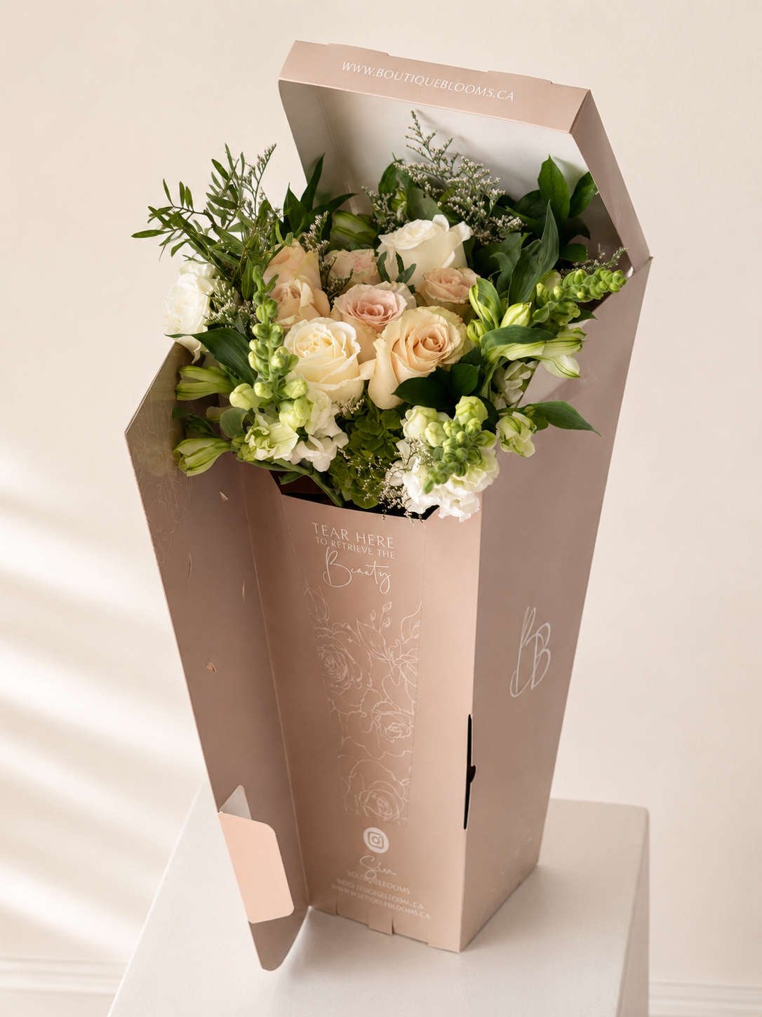 Blush and ivory roses with fresh greenery presented in a signature Boutique Blooms flower bag for Toronto delivery.