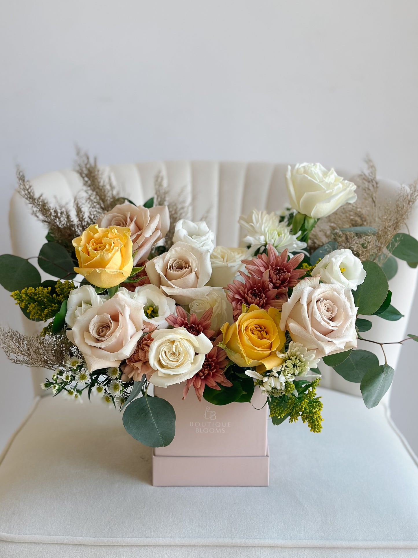 Golden yellow and champagne roses paired with ivory blooms, eucalyptus, and seasonal florals in a luxury Boutique Blooms box.