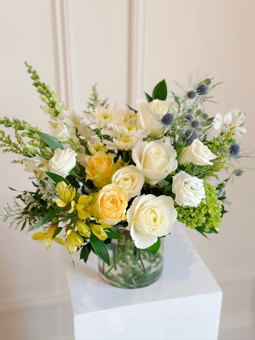 A vibrant floral arrangement featuring a mix of yellow and white flowers in a clear glass vase, set against a neutral background.