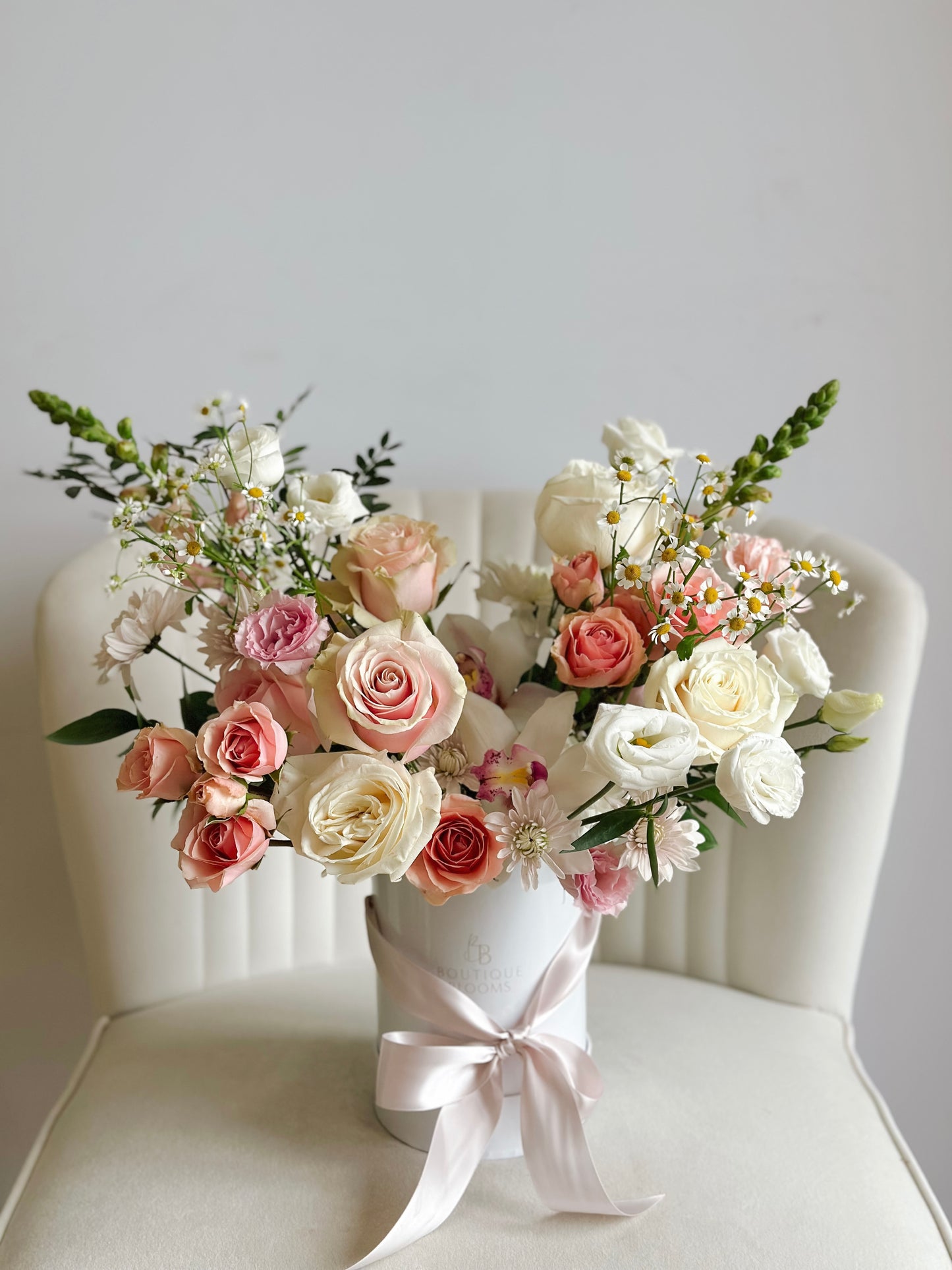 Bouquet of pink and white roses in a white vase on a white chair with a light gray background