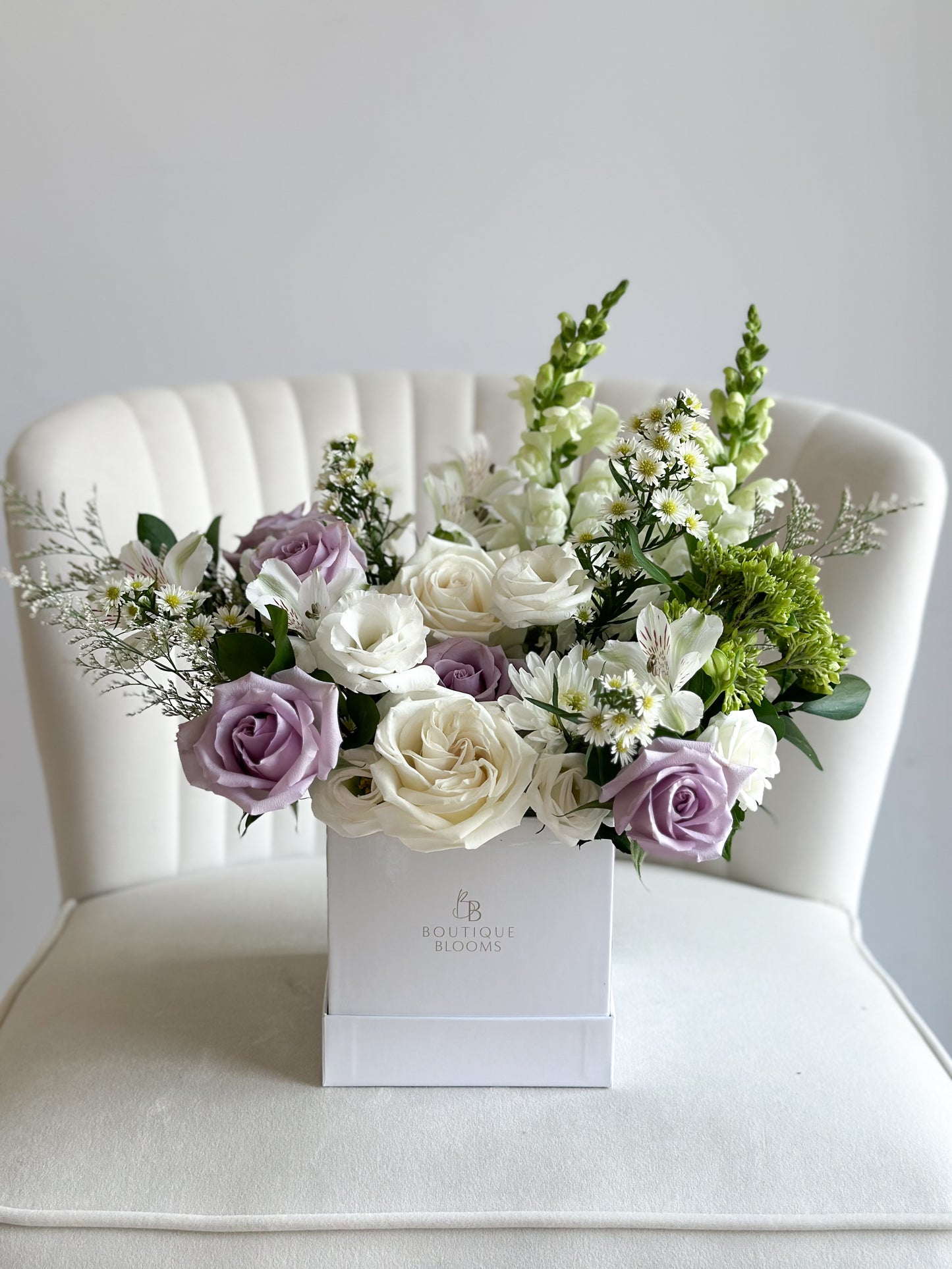 Lavender roses, ivory garden roses, white lisianthus, snapdragons, and delicate seasonal florals arranged in a luxury flower box.
