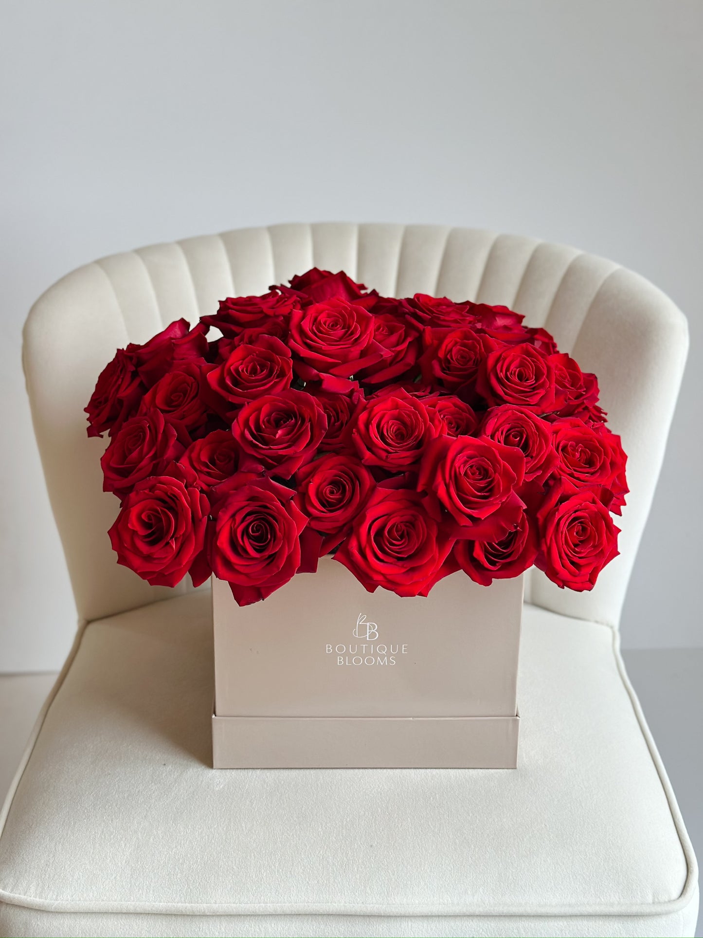 Box of red roses on a white chair with a light gray background