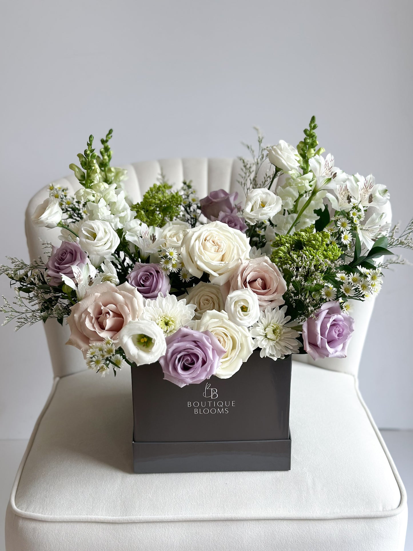 Lavender, ivory, and blush roses paired with white lisianthus, snapdragons, and garden florals in a luxury Boutique Blooms box.