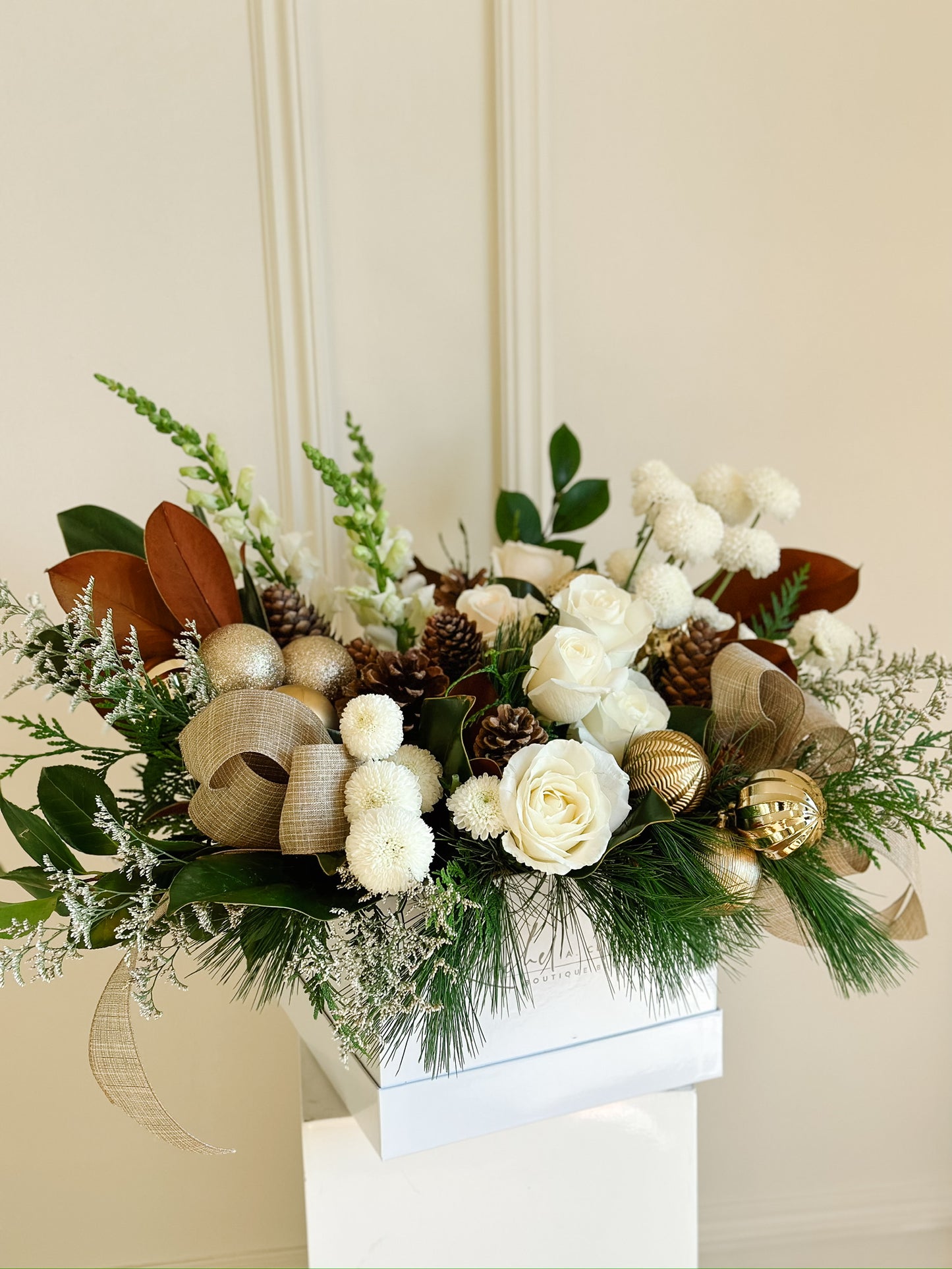 a white hat box filled with white flowers, gold ribbon, gold ornaments and pinecones filled with winter greenery and magnolia. 