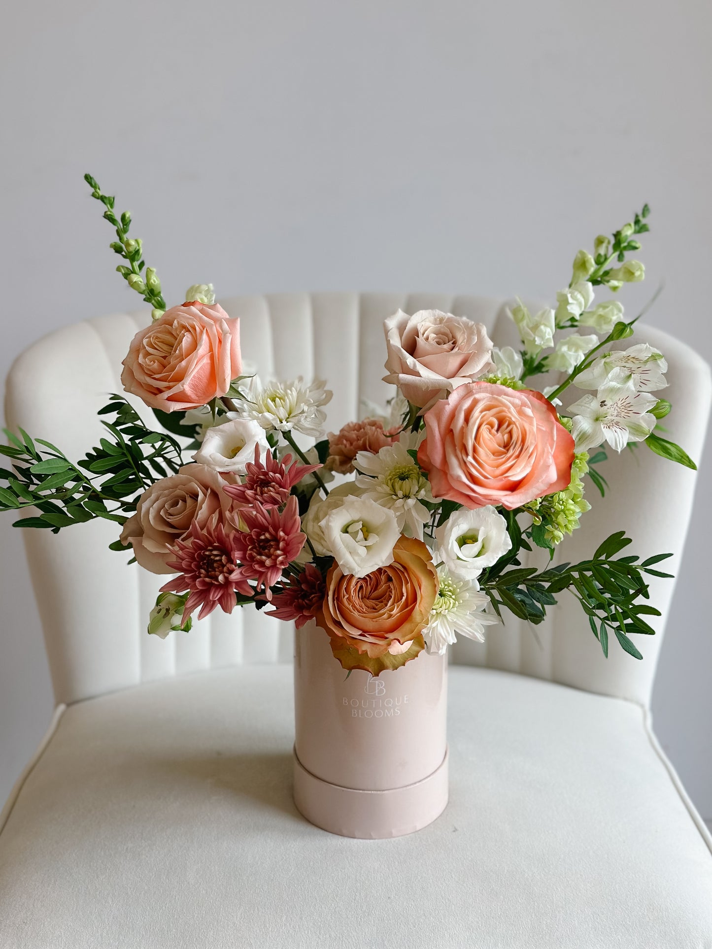Bouquet of flowers in a pink cylindrical container on a white chair.