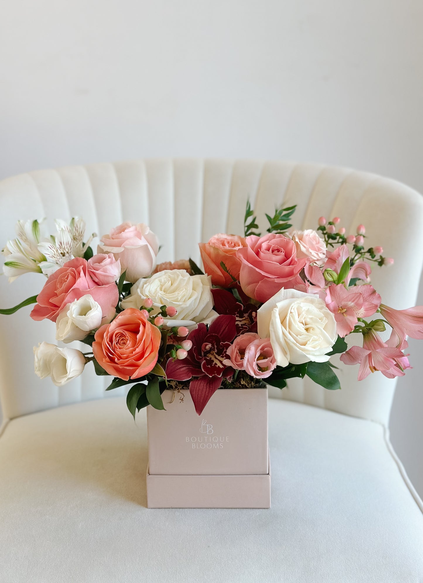 Bouquet of pink, white, and red flowers in a box on a white chair.