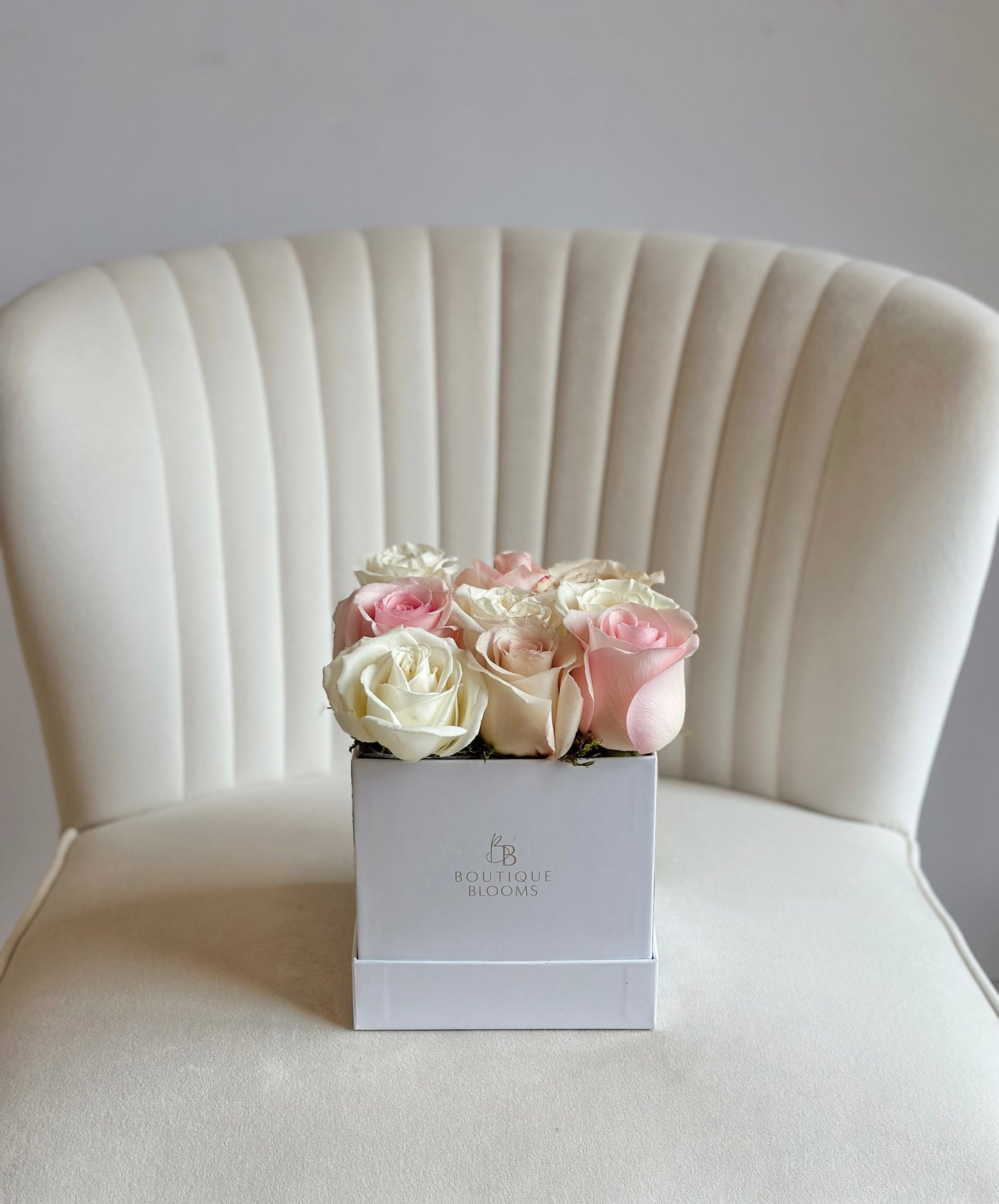 Box of pink and white roses on a white chair with a plain background