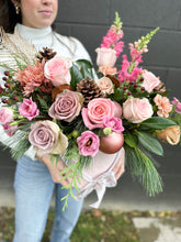 Load image into Gallery viewer, a hat box of flowers featuring roses, snap dragons, mums, winter greenery, as well as pinecones and christmas ornaments.
