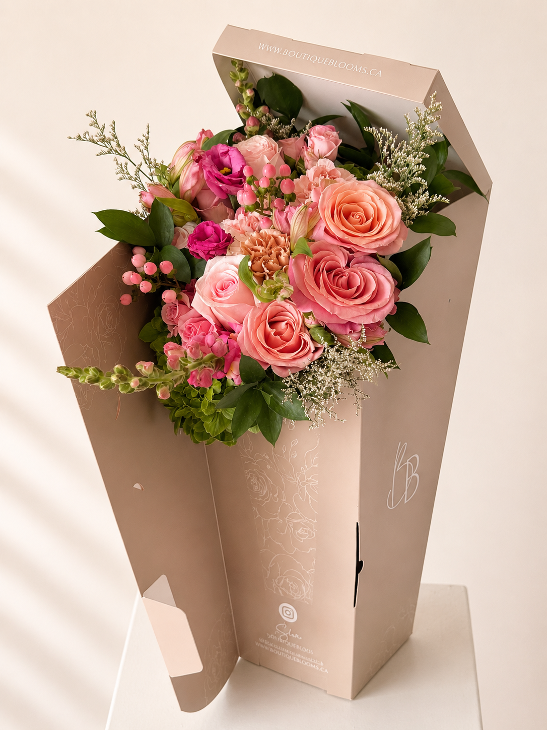 Pink roses, spray roses, lisianthus, and seasonal blooms arranged in a signature Boutique Blooms floral gift bag.