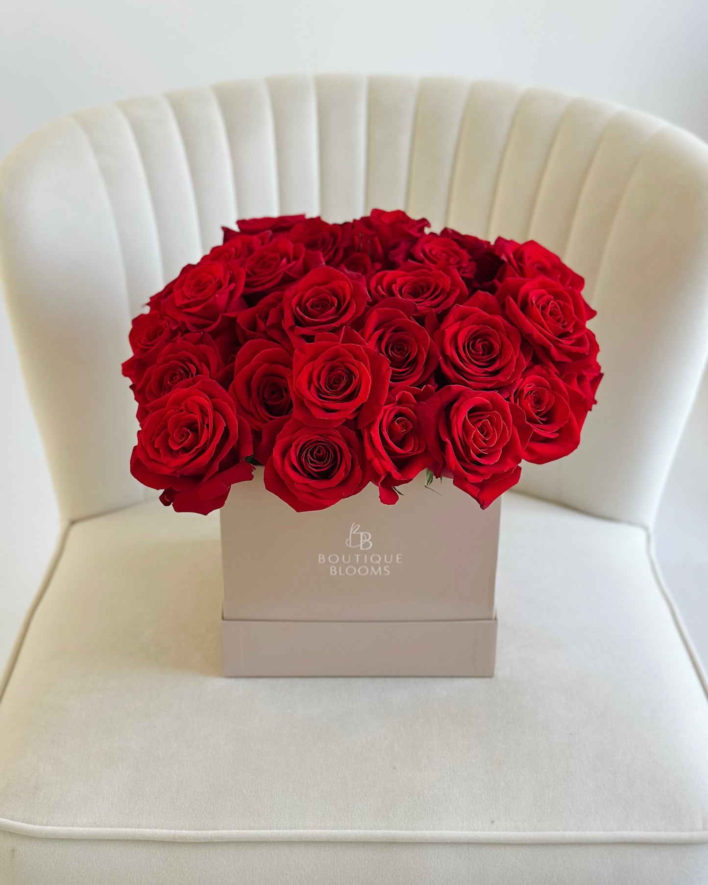 Box of red roses on a white chair with 'Boutique Blooms' branding.