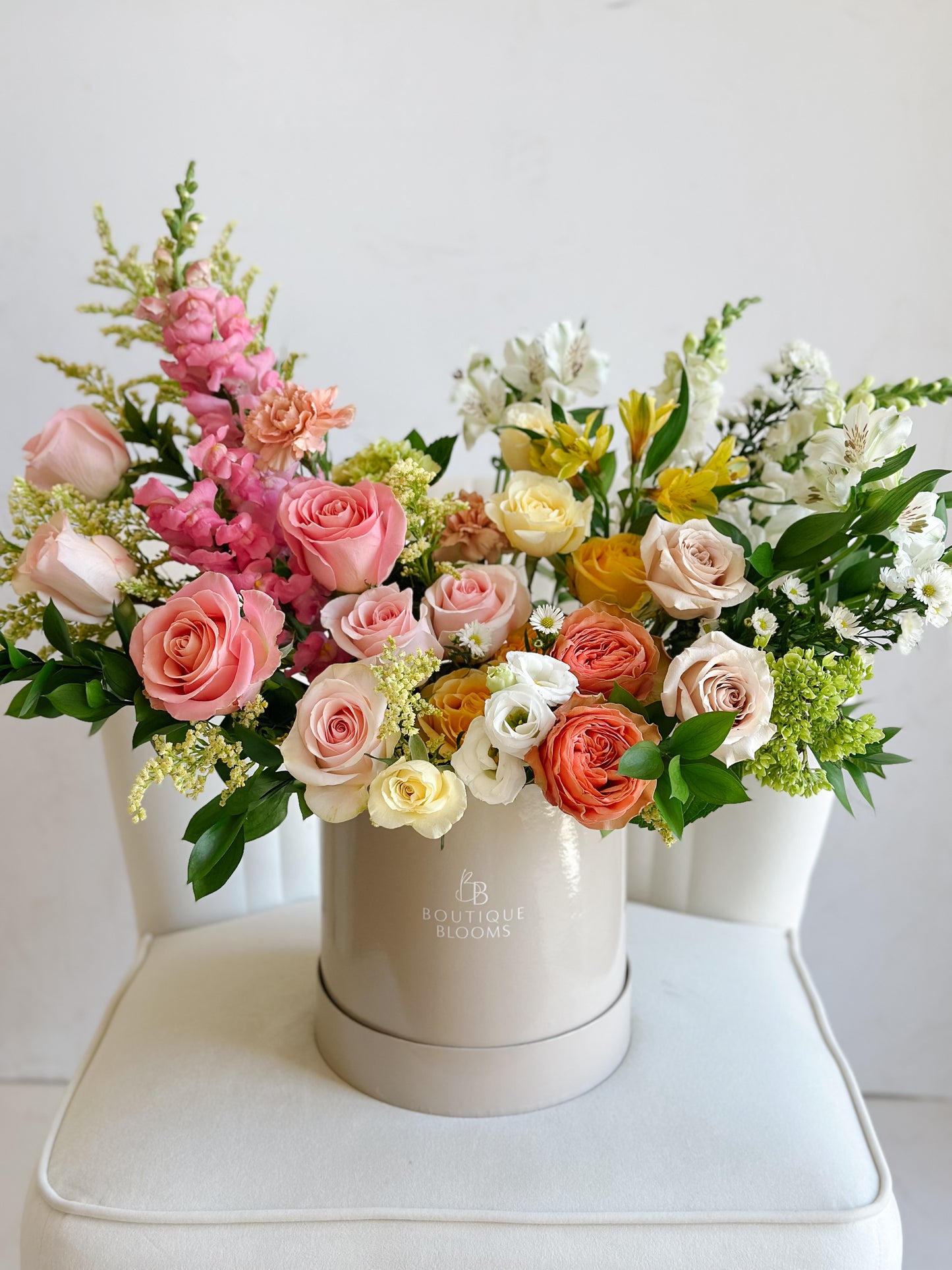 Pink, peach, yellow, and ivory roses arranged in a luxury floral hat box with seasonal summer blooms.
