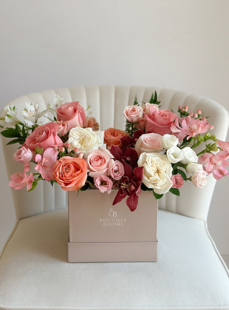 Pink and coral roses, ivory garden roses, burgundy orchids, and blush seasonal blooms arranged in a luxury Boutique Blooms flower box.