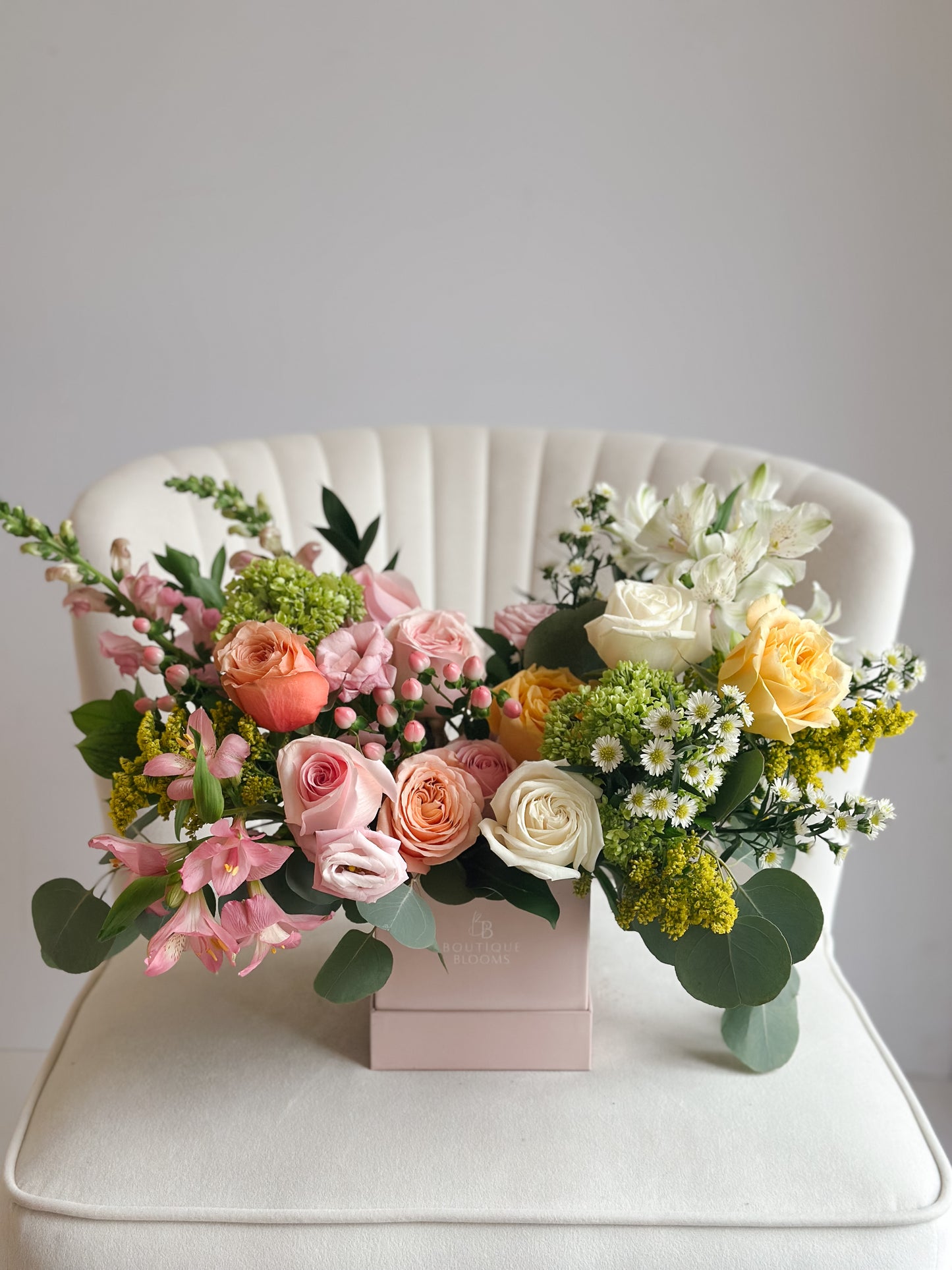 Floral arrangement in a box on a white chair with a light gray background