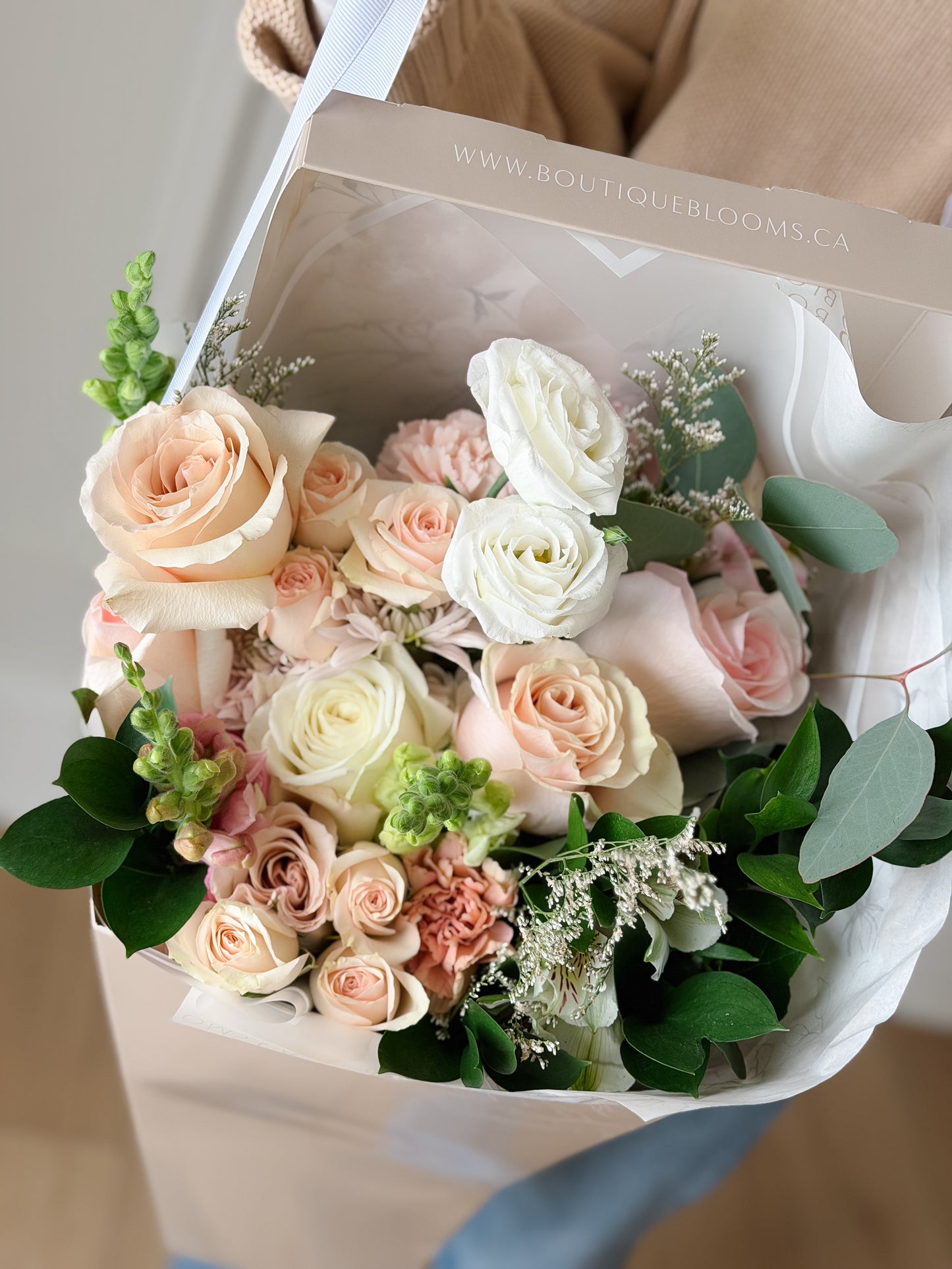 Blush and ivory roses arranged in a luxury flower bag with fresh greenery for Toronto flower delivery.