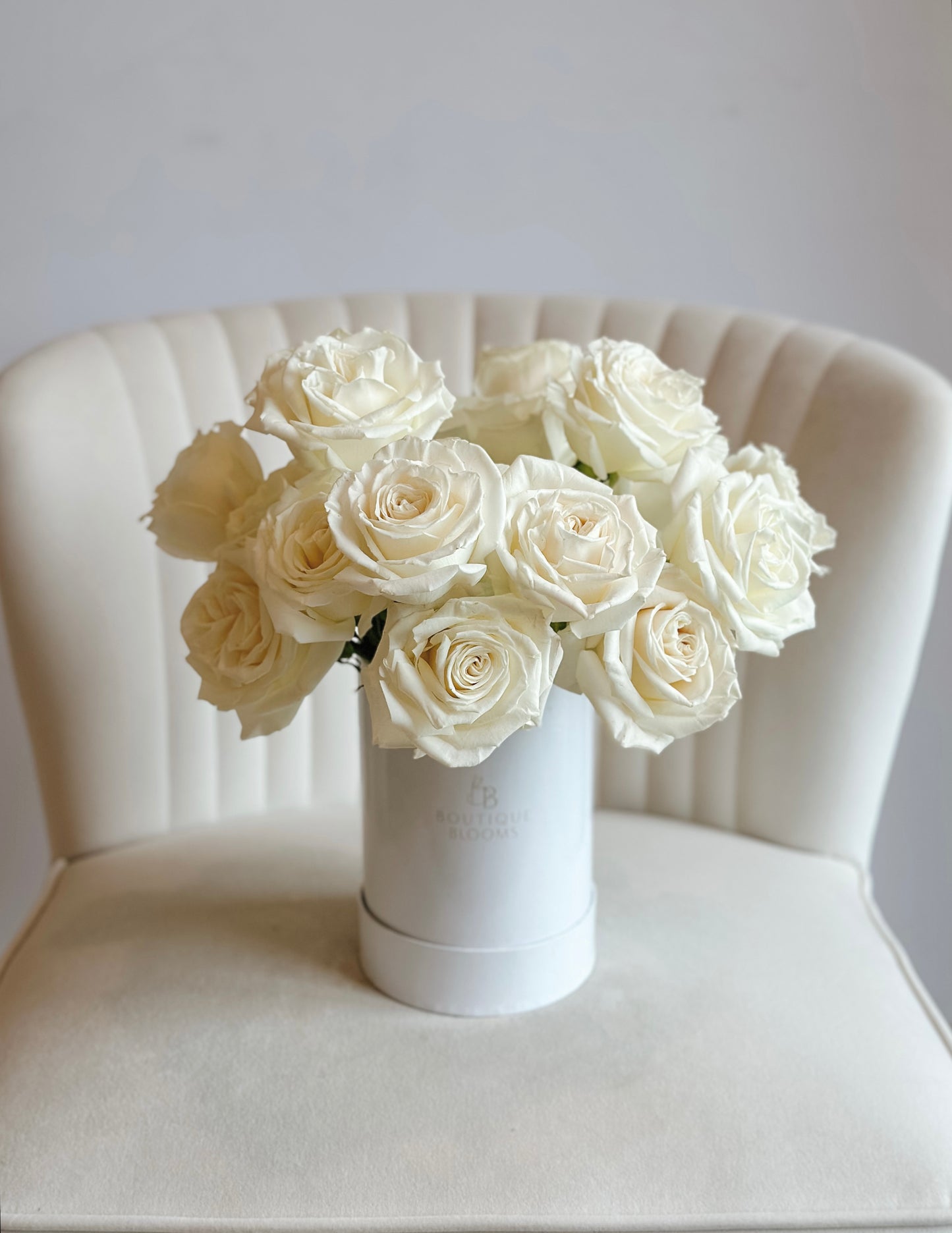 White roses in a vase on a white chair with a light gray background