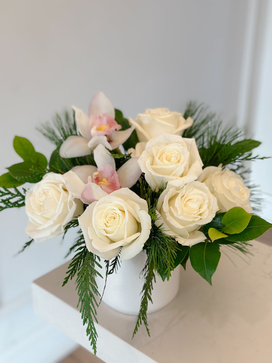 Bouquet of white roses and pink orchids in a white vase on a light surface.
