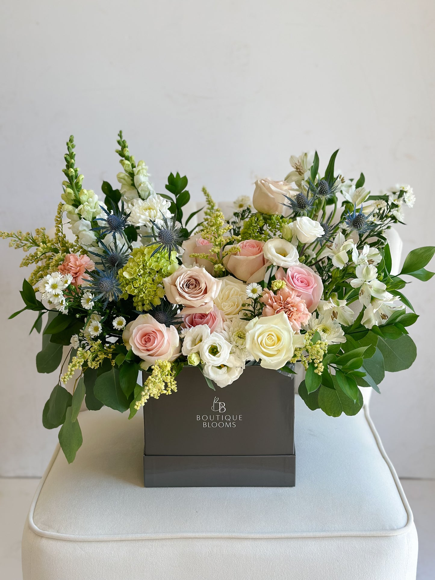 Floral arrangement in a box with 'Boutique Blooms' branding on a white surface.