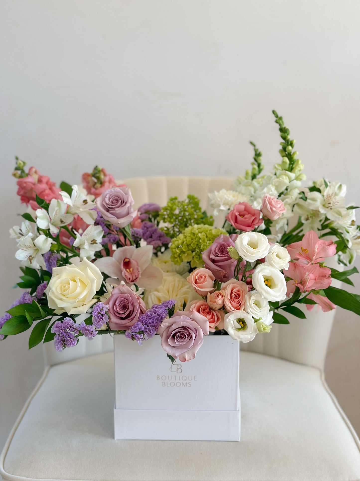 Lavender roses, white lisianthus, orchids, and blush spray roses arranged in a modern Boutique Blooms floral box.