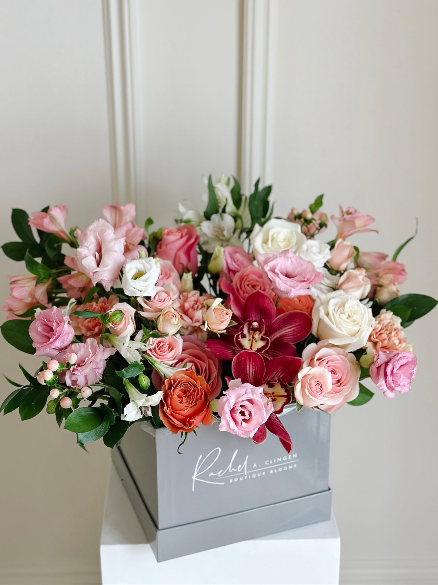 A floral arrangement with a variety of pink, red, and white flowers in a rectangular gray container with the brand name 'Rita' on the side.