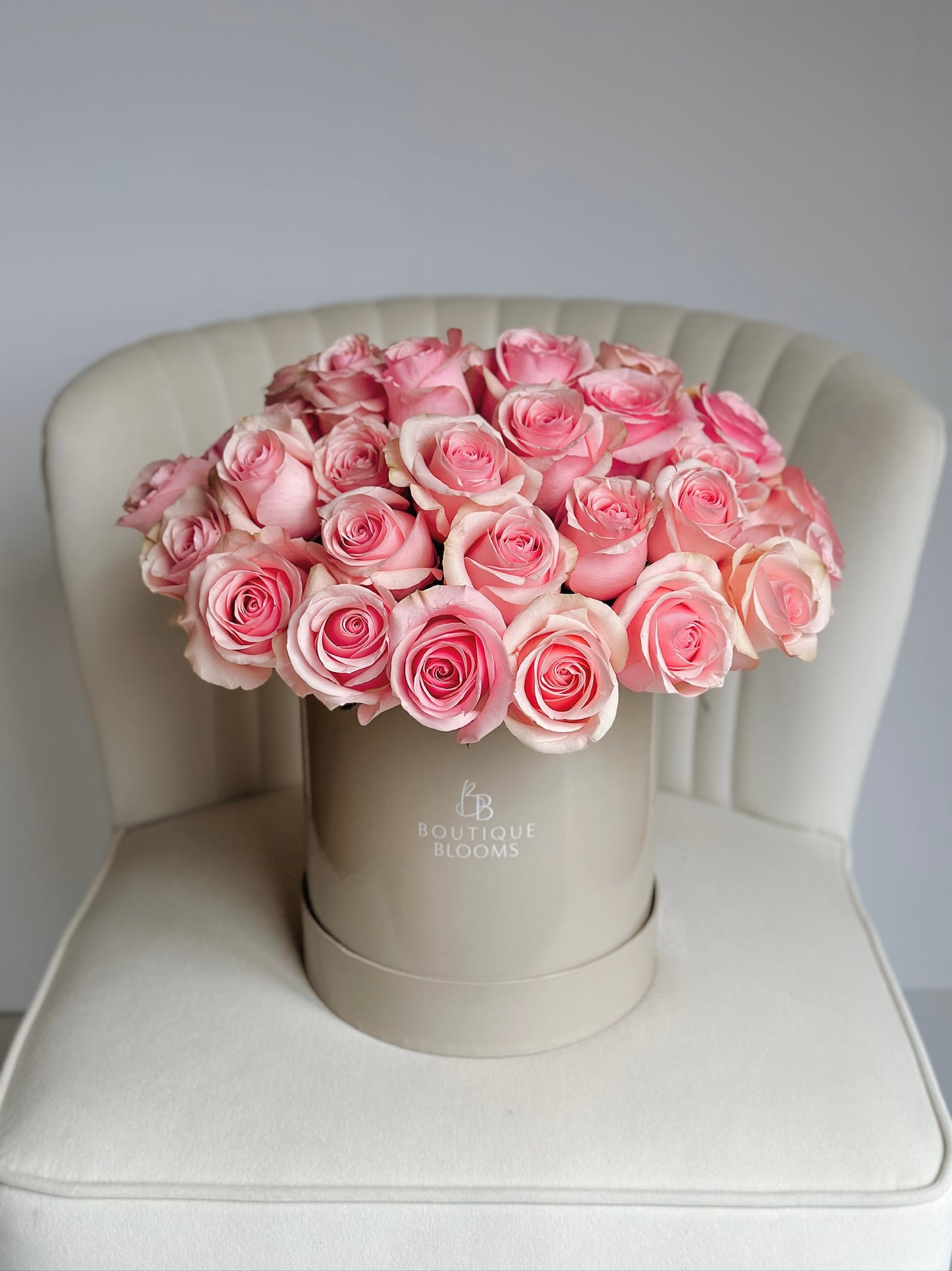 Bouquet of pink roses in a beige box on a white chair with a light gray background