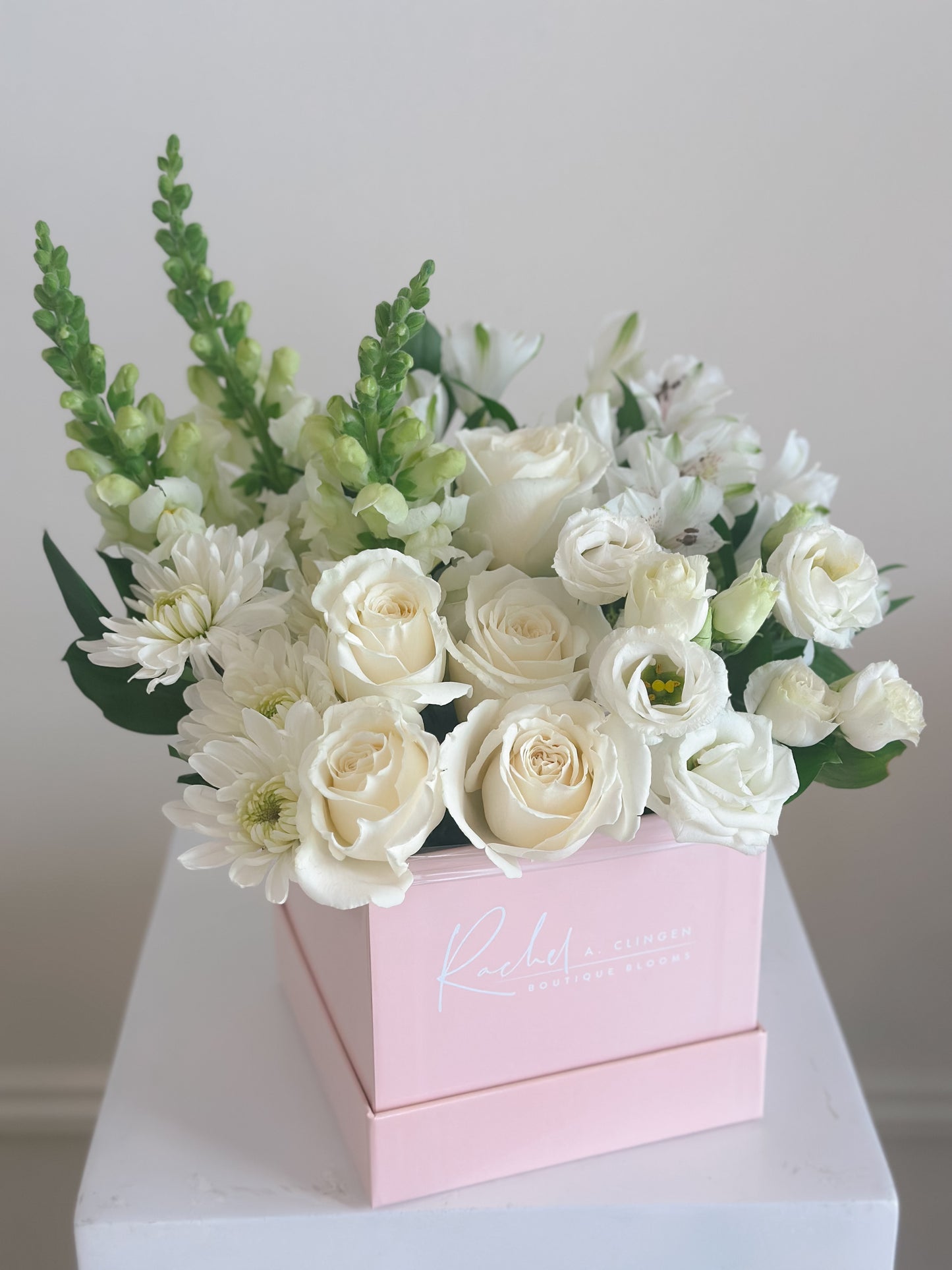 A collection of white flowers grouped by flower variety designed in a pink square box.