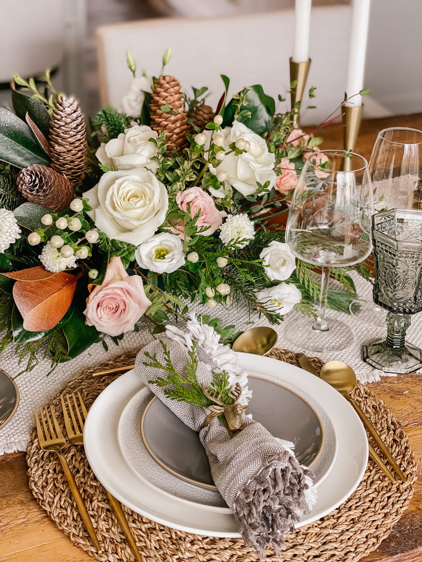 A floral centerpiece featuring a mix of fresh roses, winter berries, and pine cones, arranged on a table with holiday decor.