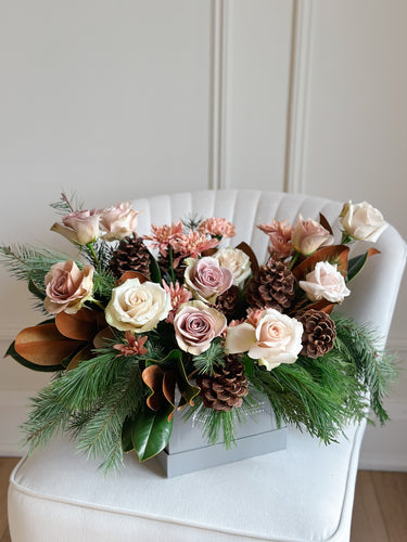 a winter flower arrangement with quicksand roses, winter greenery, and pinecones. 