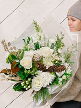 Load image into Gallery viewer, a hand tied flower bouquet featuring white roses, magnolila and winter greens with pinecones and christmas ornaments.
