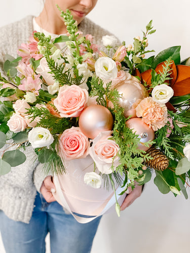 pink round box filled with white and pink flowers with christmas greenery and pink ornaments.